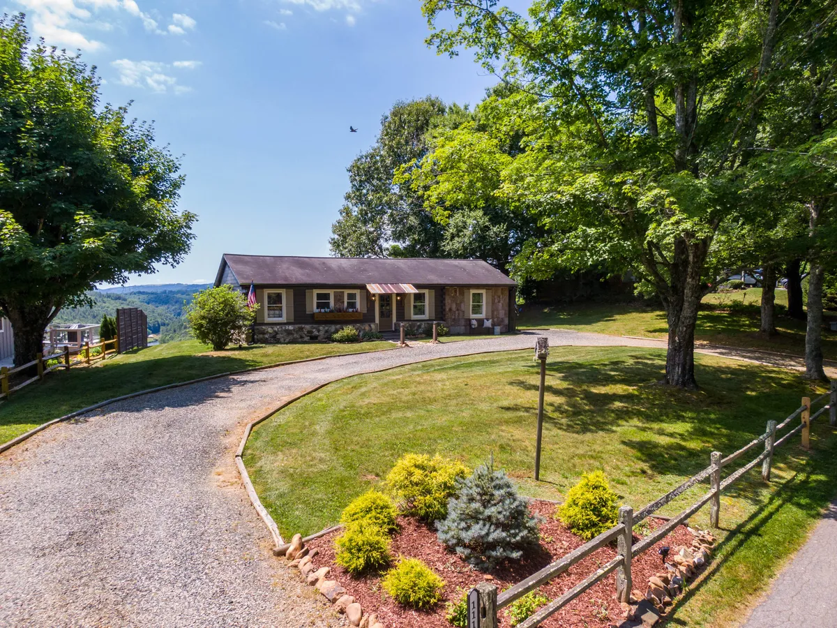A wide shot of the house reveals a landscaped garden and a spacious driveway, all set against the backdrop of green hills. The home’s exterior looks warm and welcoming, with plenty of room for outdoor activities.
