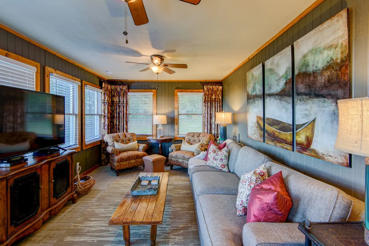 A spacious and comfortable living room centered around a sofa, with armchairs, a coffee table, television, and artwork. The arrangement is ideal for socializing, watching movies, or enjoying a quiet afternoon, and the room is bathed in natural light, enhancing the communal atmosphere.