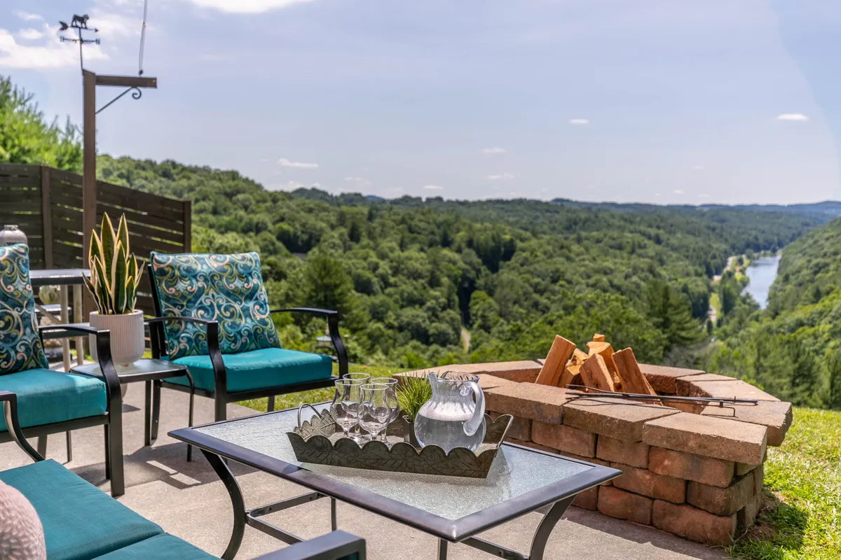 A cozy outdoor seating area with comfortable chairs encircling a fire pit, all set against a serene river backdrop. The tranquil mood and inviting setup suggest both daytime relaxation and evening stargazing.