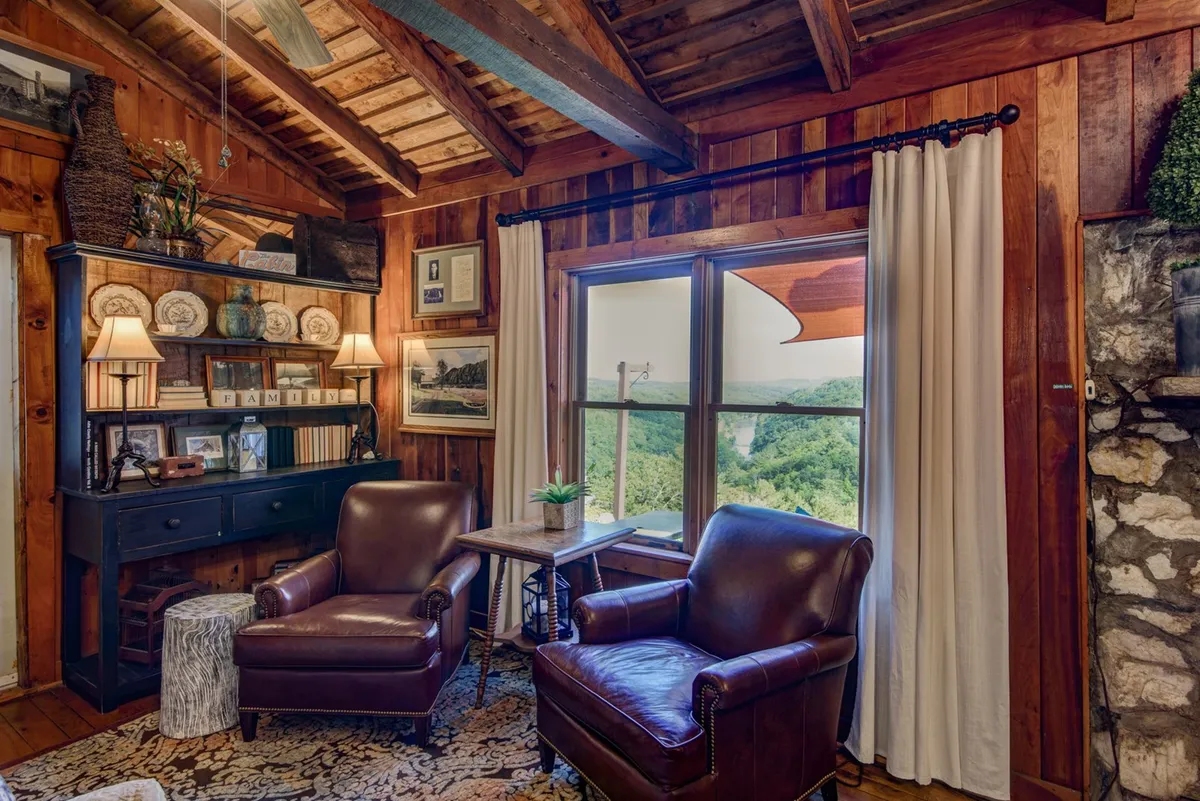 A warm and inviting living area featuring leather chairs, a wooden bookshelf, and a large window that frames a scenic view. The space encourages both relaxing with a book and conversing with friends while also offering a cozy spot to watch the sunset around the electric fireplace.
