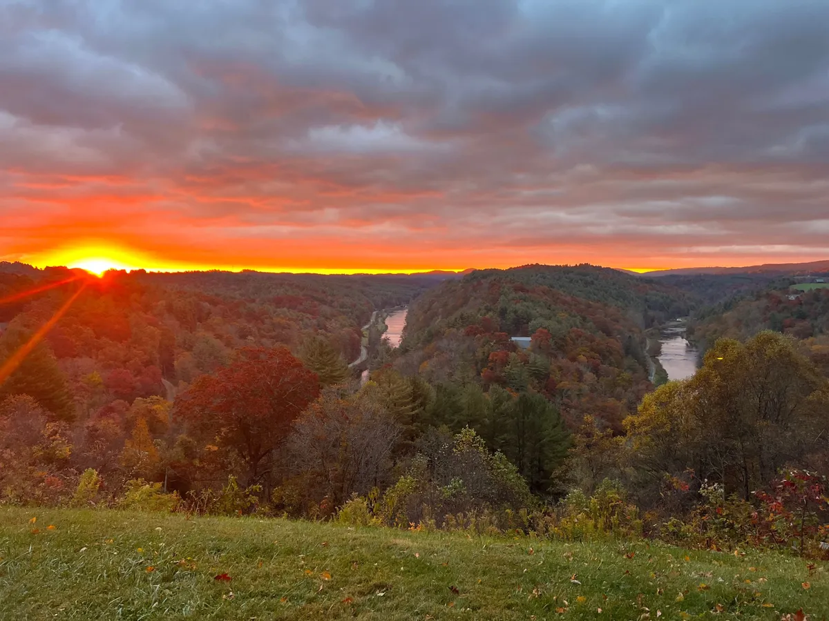 A sweeping, tranquil view of the river at sunset, framed by lush foliage and rolling hills. The scene evokes a sense of peaceful seclusion and natural beauty, perfect for romantic moments or nature appreciation. The colors and landscape invite photography, quiet reflection, or simply soaking in the panorama together.