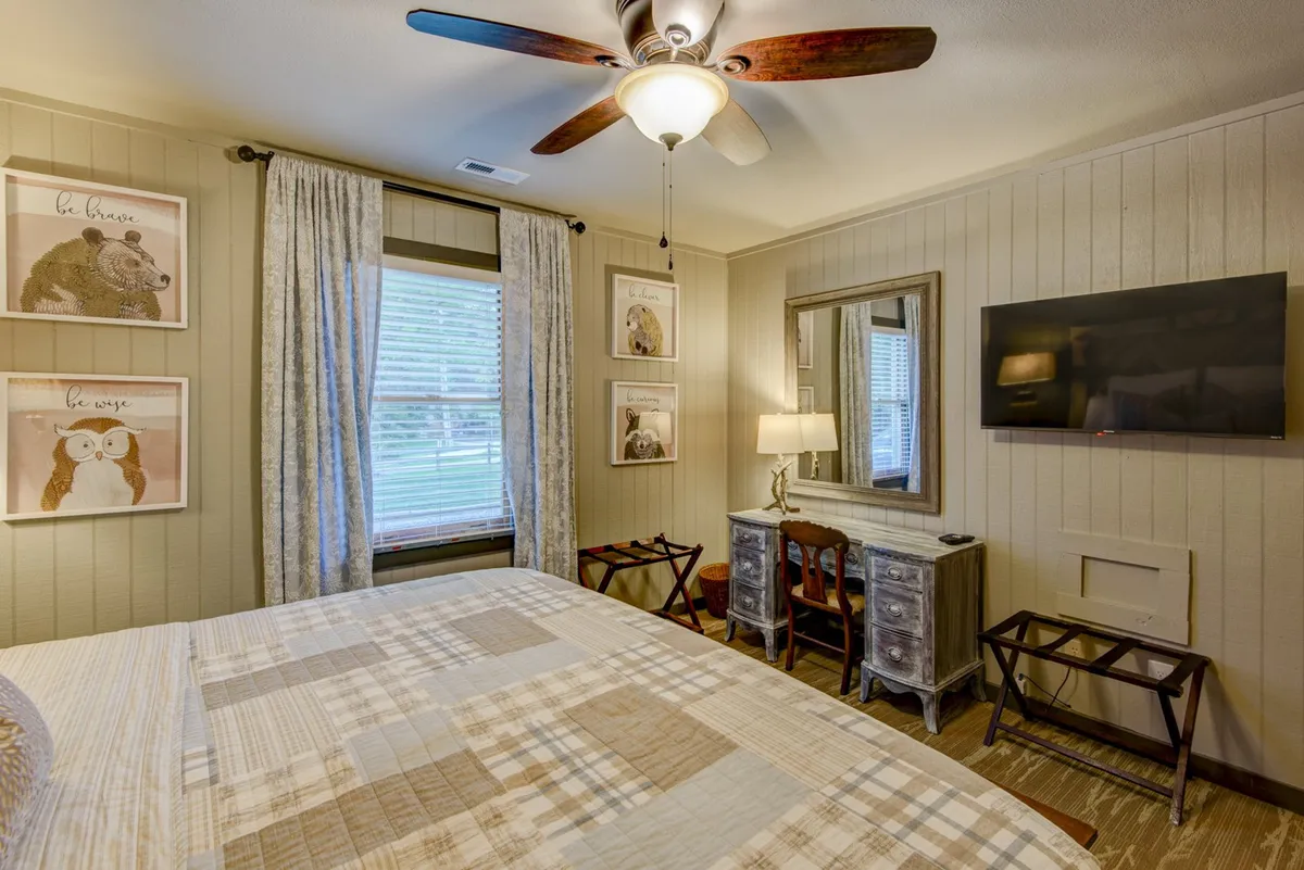 A comfortable bedroom featuring a bed with patterned bedding, framed animal artwork, wooden furniture, and a ceiling fan with light. The space feels warm, inviting, and perfectly suited for family or friends traveling together.