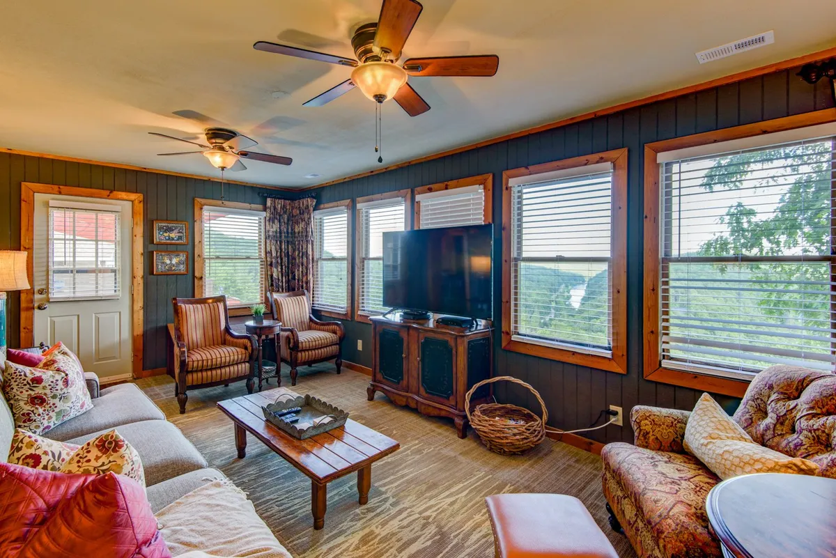 A bright and welcoming seating area with a comfortable couch, decorative pillows, a television, and large windows that offer expansive views. The setup is perfect for relaxing, entertaining, or simply enjoying the changing light over the landscape.