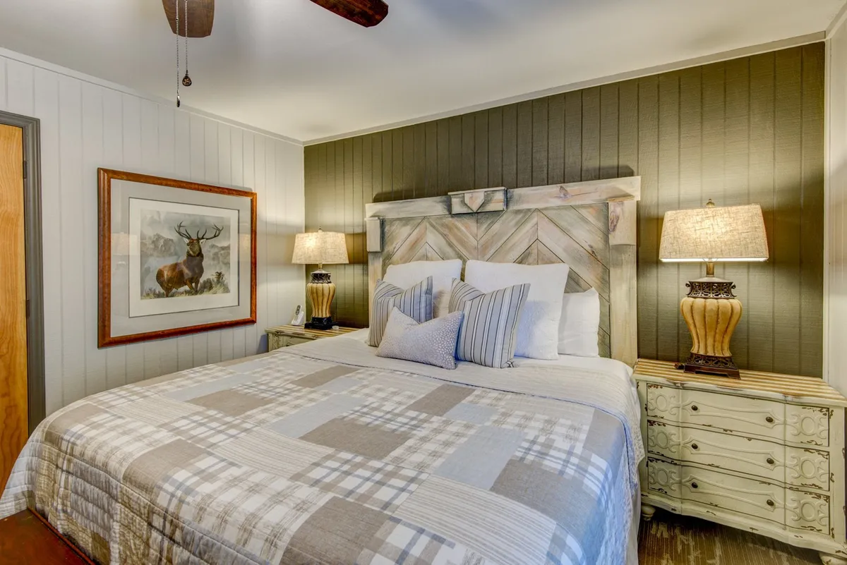 A restful bedroom scene showcasing a comfortable bed with patterned bedding, a sturdy wooden headboard, matching nightstands with elegant lamps, and framed artwork above the bed. The soft light and harmonious decor evoke a sense of privacy and relaxation.