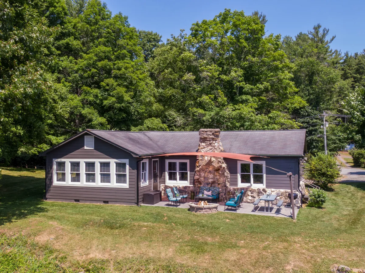 A cozy outdoor patio area with a stone chimney and seating surrounded by greenery, set up for relaxing or gathering around the fire pit. The space is inviting and intimate, ideal for morning coffee, stargazing, or quiet conversation enveloped by the sights and sounds of nature.
