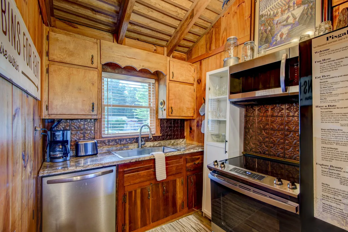 A closeup view of a kitchen sink with stainless steel appliances, wooden cabinetry, and a decorative backsplash, all bathed in warm, homey lighting.