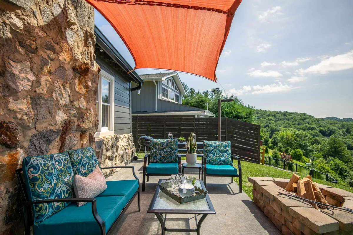 This exterior image features colorful seating, an outdoor table, a fire pit, and a decorative shade sail, all arranged to encourage socializing, relaxation, and casual family gatherings. The landscape beyond invites exploration and outdoor enjoyment, supporting a sense of togetherness in a scenic setting.